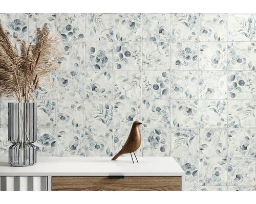 Wandfliesen mit botanischem Blattmuster in hellem Raum mit Sideboard, Glasvase und hölzernem Dekovogel.