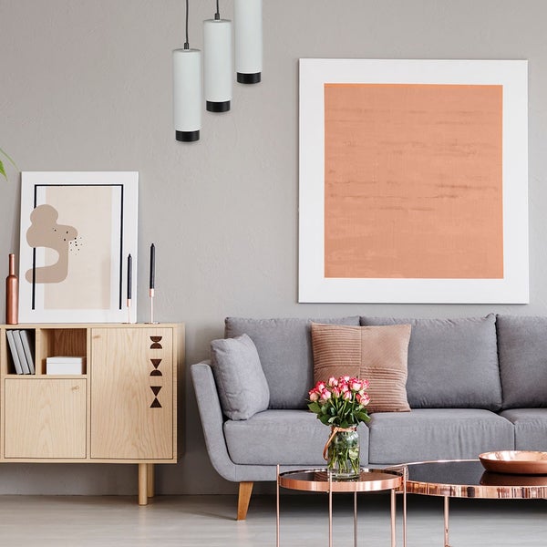 Modernes Wohnzimmer mit grauer Couch, Sideboard aus Holz und einer 3-flammigen Pendelleuchte mit weißen, zylindrischen Schirmen.