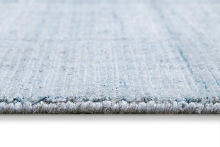 Ein moderner Teppich mit blau-grauem Linienmuster, darauf steht ein dunkler gepolsterter Hocker mit einem filigranen schwarzen Metalldrahtgestell.
