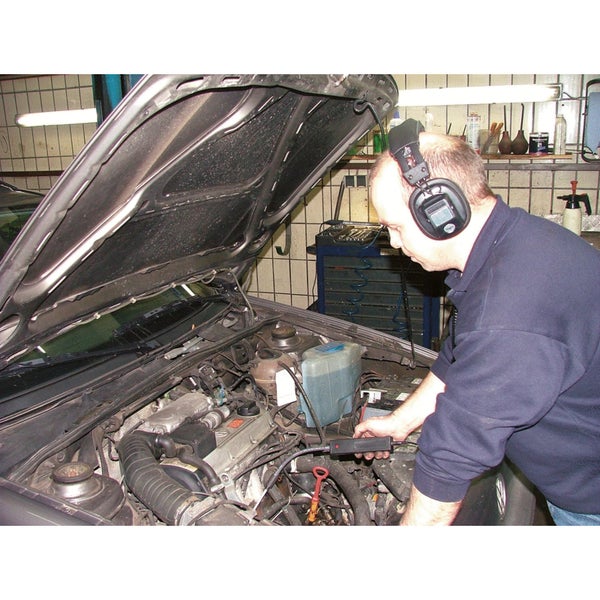 Ein Mann mit Kopfhörern diagnostiziert einen Automotor mit einem elektronischen Gerät.
