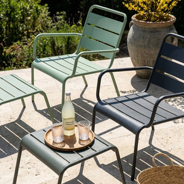 Moderne Gartenmöbel aus Metall auf einer hellen, organisierten Terrasse, bestehend aus zwei Sesseln mit Lamellen und passenden Beistelltischen.