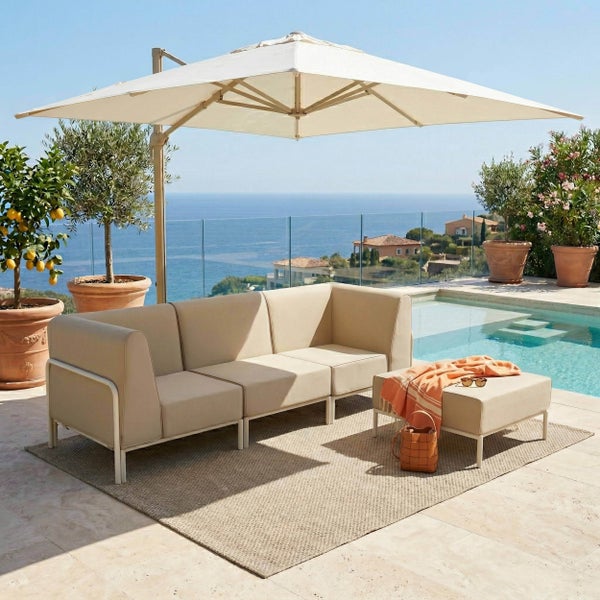 Moderne Garten-Lounge mit Sofa, Hocker und Sonnenschirm auf einer hellen Terrasse am Pool mit Meerblick.