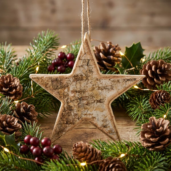 Hängender Stern aus Birkenrinde umgeben von einem weihnachtlichen Kranz mit Tannenzweigen, Tannenzapfen, roten Beeren und Lichterkette.