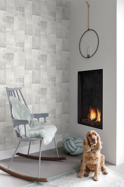 Wohnraum mit gemusterter Tapete, Schaukelstuhl, Kamin und Hund