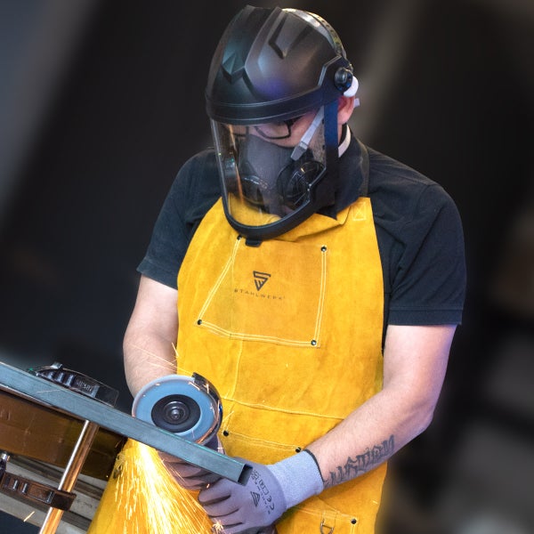 Schweißer mit Schweißhelm, Atemschutzmaske und Lederschürze bei der Arbeit mit einem Winkelschleifer.