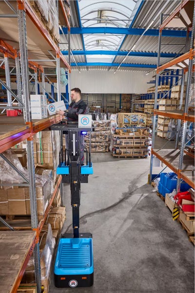 Ein Mitarbeiter bedient einen elektrischen Vertikal-Kommissionierer in einem Lagerhaus mit hohen Regalen.