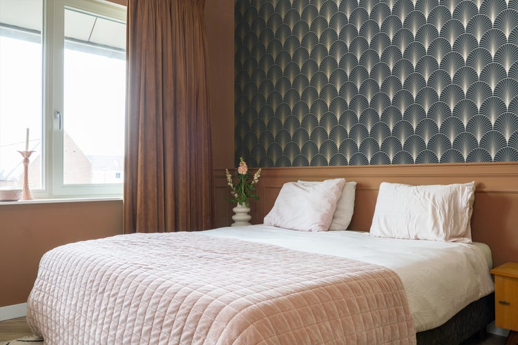 Schlafzimmer mit Bett, Nachttisch und gemusterter Tapete