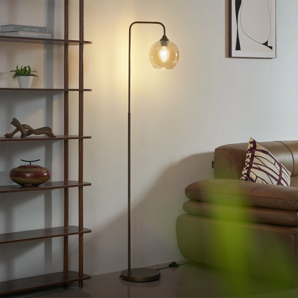 Moderne Stehleuchte mit kugelförmigem Glasschirm in einem Wohnzimmer neben einem dunklen Holzregal und einem Sofa.