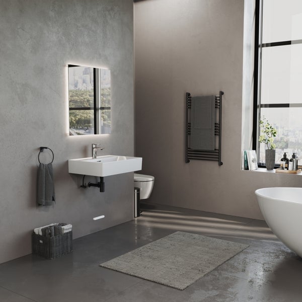 Modernes Badezimmer im Industriestil mit grauem Betonlook, wandhängendem Waschbecken, beleuchtetem Spiegel und schwarzem Handtuchheizkörper.