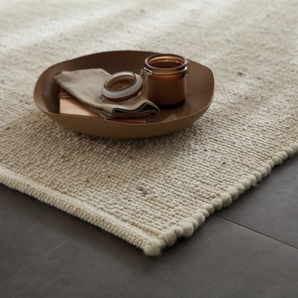 Dekoratives Arrangement auf einem gewebten Teppich mit Schale, Stoff und Glas