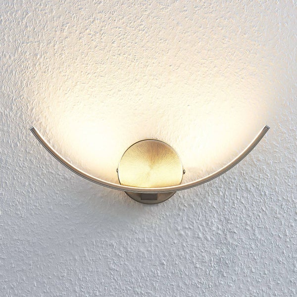 Moderne, gebogene LED-Wandleuchte in Messing-Optik mit indirektem Licht nach oben an einer strukturierten Wand.