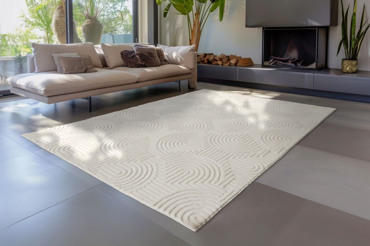 Moderner Wohnzimmerteppich mit strukturiertem Kreisbogenmuster auf flachem Boden vor einem Sofa in einem hellen, elegant eingerichteten Wohnbereich.