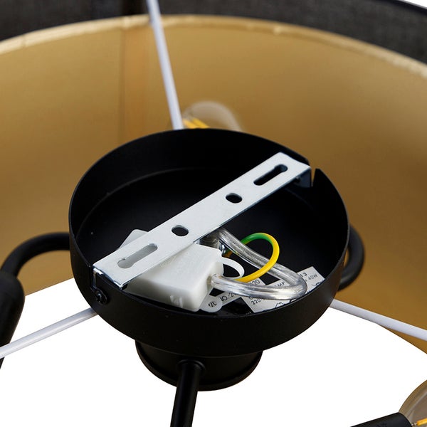 Innenansicht der Deckenhalterung einer Leuchte mit Metallbügel, Lüsterklemme und Erdungskabel vor einem goldfarbenen Lampenschirm.