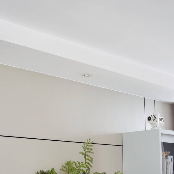 Moderner LED Einbaustrahler in einer weißen Decke über einer hellen Wand mit Farn und weißem Schrank.