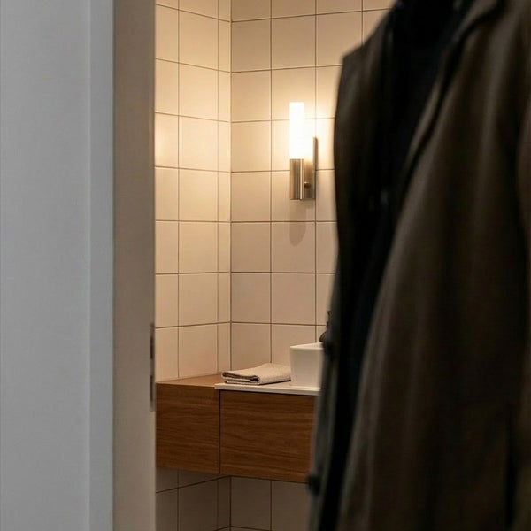 Blick durch eine Tür in ein Badezimmer mit Holzwaschtisch, Wandleuchte und quadratischen Fliesen.