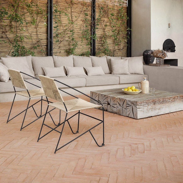 Moderne Lounge Terrasse mit Rattan Sesseln und grobem Holztisch auf einem Ziegelboden in Fischgrätoptik vor einer geflochtenen Trennwand.