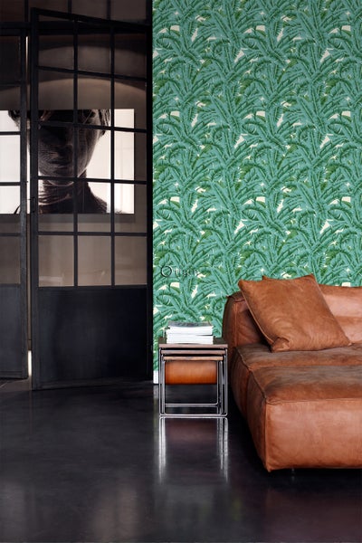 Wohnzimmer mit Palmen-Tapete, Ledersofa und Satztischen.