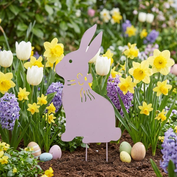 Osterhasen Gartenstecker aus Metall als Dekoration vor einem Blumenbeet mit Narzissen und Hyazinthen sowie dekorativen Ostereiern am Boden.