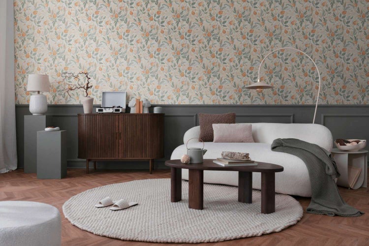 Wohnzimmer mit Vliestapete mit Blumenmuster, weißem Sofa, dunklem Holzsideboard und rundem Couchtisch auf einem hellen Teppich.