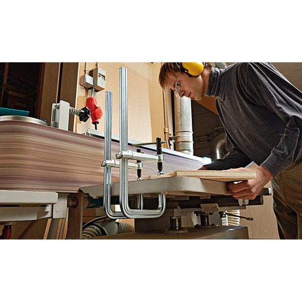 Ein Mann arbeitet mit einer Bandschleifmaschine in einer Werkstatt. Er trägt einen Gehörschutz und schleift ein Holzbrett.