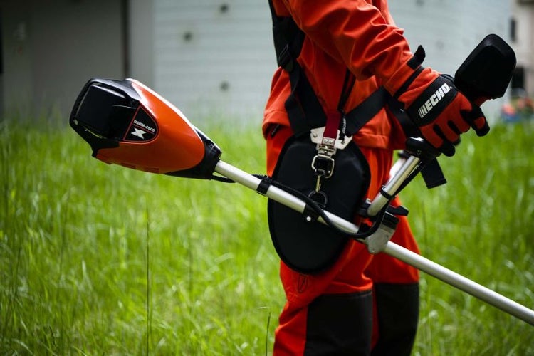 Person mit einem Rasentrimmer der Marke Echo mit Tragegurt auf einer Wiese.