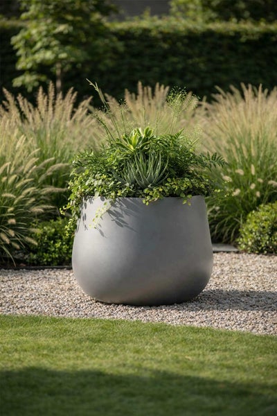 Großer runder grauer Pflanzkübel für außen, bepflanzt mit Sukkulenten und Farnen auf einer Kiesfläche im Garten.