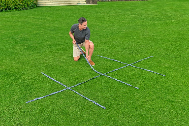 Ein Mann kniet auf dem Rasen und legt Markierungsbänder in einem Gittermuster aus, um ein Gartenprojekt zu planen.