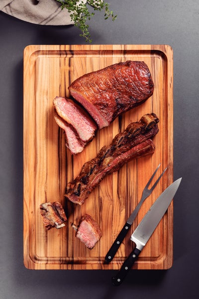 Holzschneidebrett mit gebratenem Fleisch, Gabel und Messer