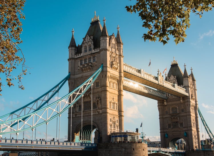 Wandbild der Londoner Tower Bridge mit steinernen Türmen und blauen Hängekabeln vor einem sonnigen Himmel.