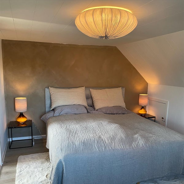 Modernes Schlafzimmer mit Doppelbett, grauem Kopfteil, braun strukturierter Wand, großer runder Deckenleuchte und zwei Tischlampen auf Nachttischen.