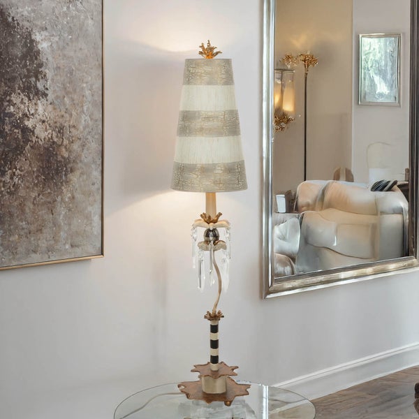 Dekorative Tischleuchte mit gestreiftem Lampenschirm auf einem Glastisch neben einem Spiegel und einem Gemälde.