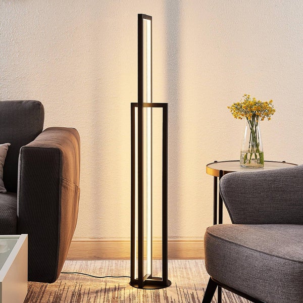Moderne schwarze LED-Stehleuchte in geometrischem Design in einem hellen Wohnzimmer mit grauem Sofa und Sessel.