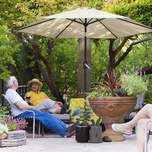 Sonnenschirm über einem Gartentisch und Stühlen aus Holz auf einer Holzterrasse im Garten vor einem Haus.