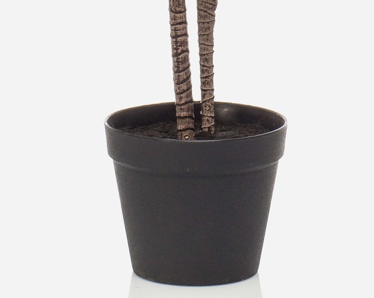 Kunstpflanze im anthrazitfarbenen Topf mit zwei strukturierten Stämmen und dunkler Erde.