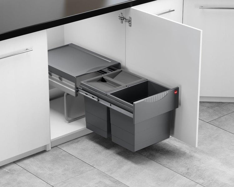 Ausziehbarer Abfallsammler mit zwei grauen Mülleimern in einem weißen Küchenunterschrank auf Schienen montiert.