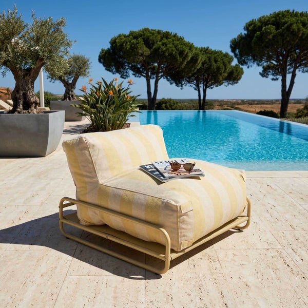 Moderner Outdoor-Loungesessel mit gelb gestreiftem Kissen auf Metallgestell an einem Pool auf einer hellen Steinterrasse mit Bäumen.