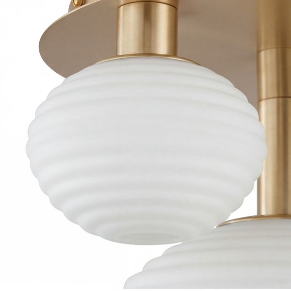 Detailansicht einer Deckenleuchte mit geriffeltem Glasschirm in Weiß und einer Halterung aus Metall in gebürstetem Messing.