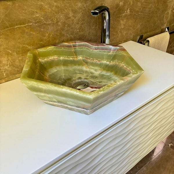 Sechseckiges Aufsatzwaschbecken aus Onyx auf einem weißen Waschtischunterschrank mit verchromter Armatur.
