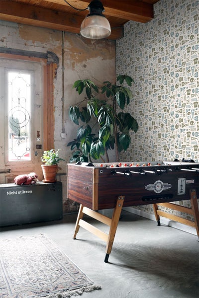 Wohnraum mit Fußballtisch, Pflanze, Kiste und gemusterter Tapete