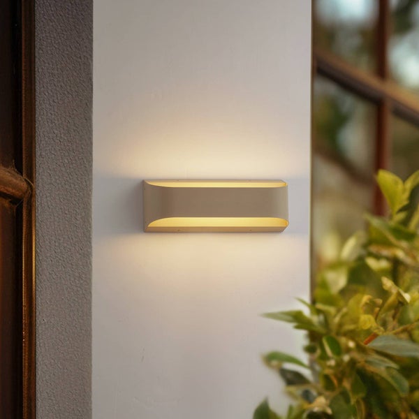 Moderne rechteckige Außenwandleuchte aus Metall mit hellem Lichtaustritt nach oben und unten an einer Fassade neben einer Pflanze.