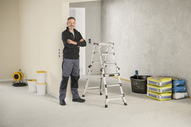 Innenraum mit Handwerker, Leiter, Farbeimern und Säcken mit Spachtelmasse