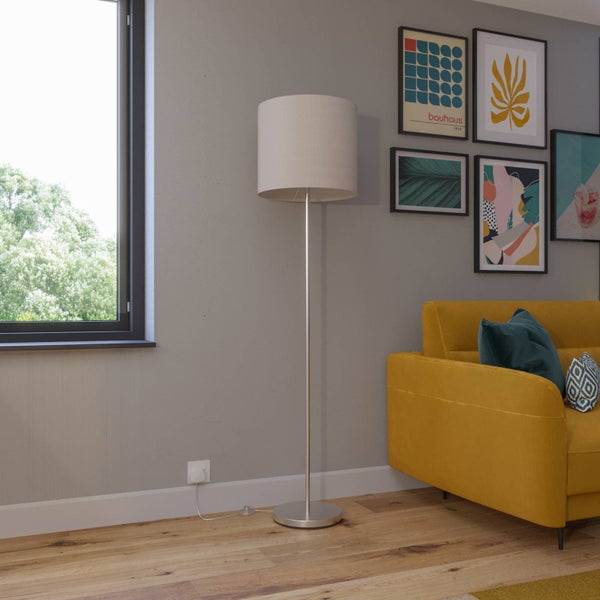Moderne Stehleuchte mit Metallfuß und beigem Stoffschirm in einem hellen Wohnzimmer neben einem Sofa und gerahmter Wandkunst.