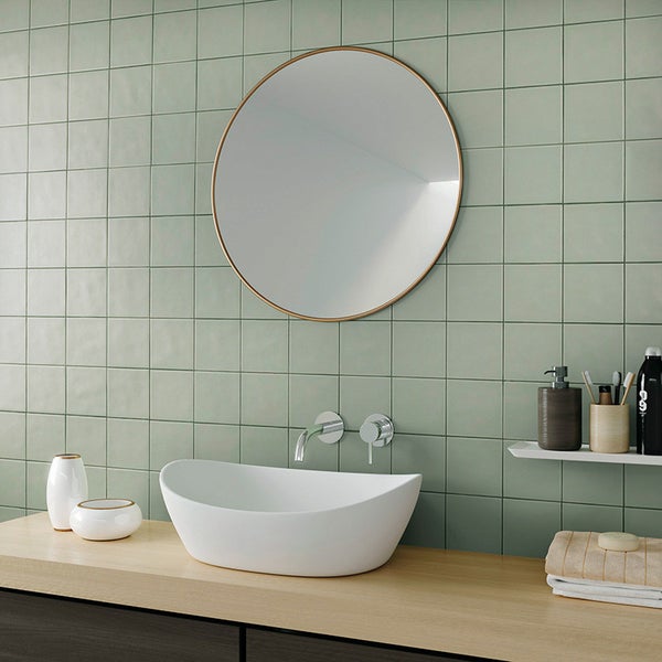 Modernes Badezimmer mit rundem Wandspiegel, Aufsatzwaschbecken und Wandarmatur vor quadratischen Fliesen auf einer Holzwaschtischplatte.