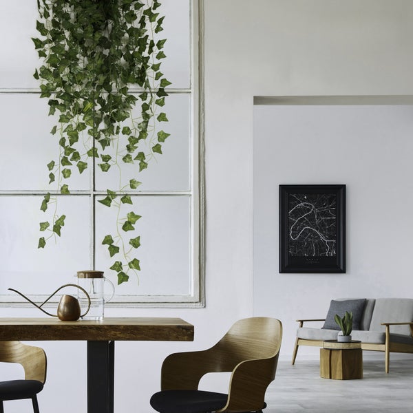 Moderner heller Raum mit Holztisch, Holzstühlen, Glaskaraffe, Gießkanne, künstlichem hängendem Efeu, Sofa und Wandbild im Hintergrund.