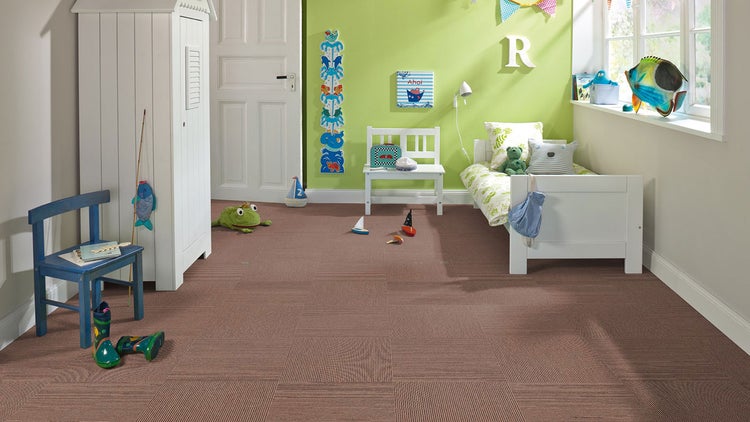 Kinderzimmer mit braunen Teppichfliesen, weißem Holzbett, Schrank und Bank, blauem Stuhl sowie hellgrüner Wanddekoration.