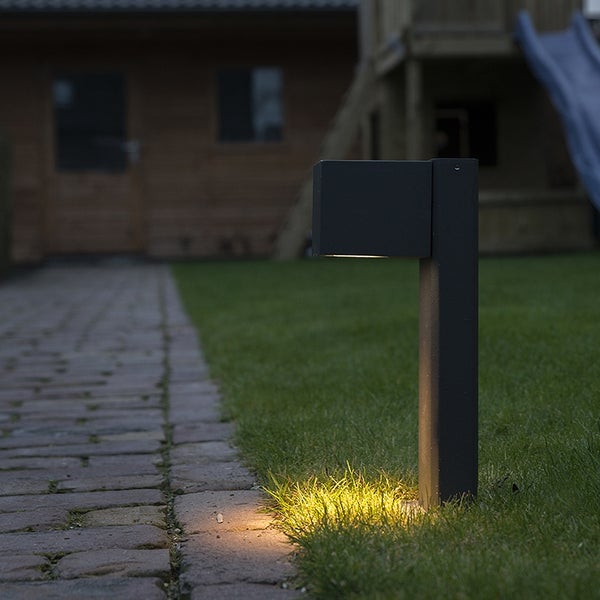 Anthrazitfarbene LED-Wegeleuchte im modernen Design beleuchtet einen Rasen und einen gepflasterten Gartenweg bei Dämmerung.