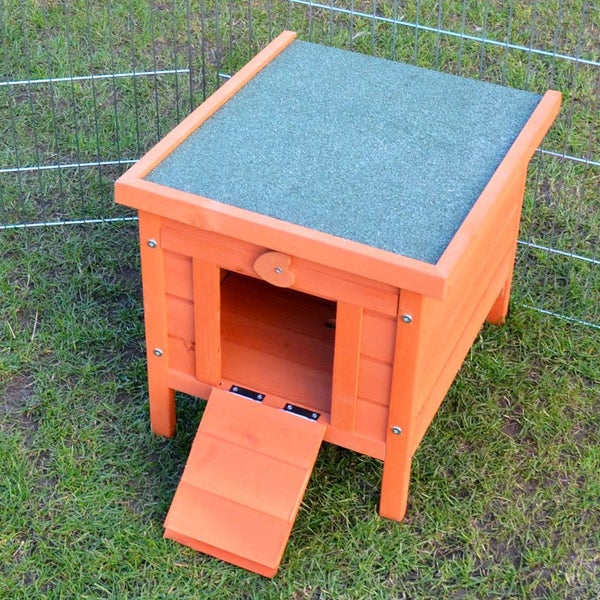 Orangefarbenes Kleintierhaus aus Holz mit grünem Bitumendach und Rampe für Kaninchen auf einer Rasenfläche im Freigehege.