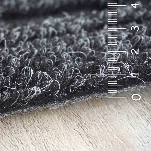 Detailansicht einer grauen Teppichfliese mit Messskala zur Darstellung der Florhöhe