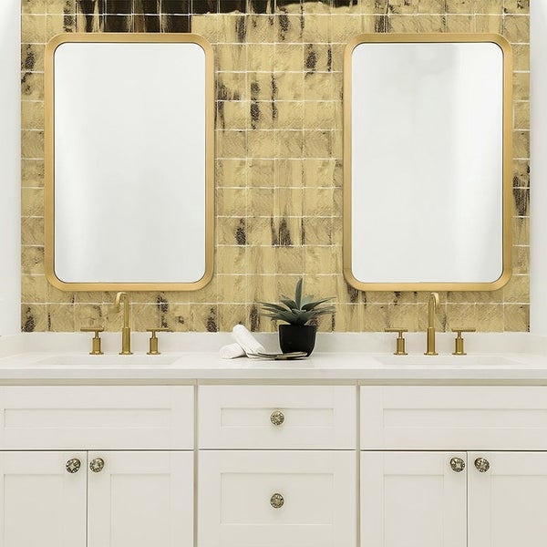 Badezimmer mit Doppelwaschtisch, zwei Spiegeln mit abgerundeten Ecken und Wandfliesen in Metallicoptik mit goldenen Akzenten.