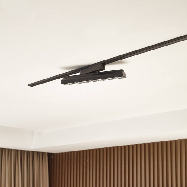Lineare schwarze LED-Leuchte in einem Magnetschienen-System an der Decke, modern gestalteter Raum mit Holzwand.